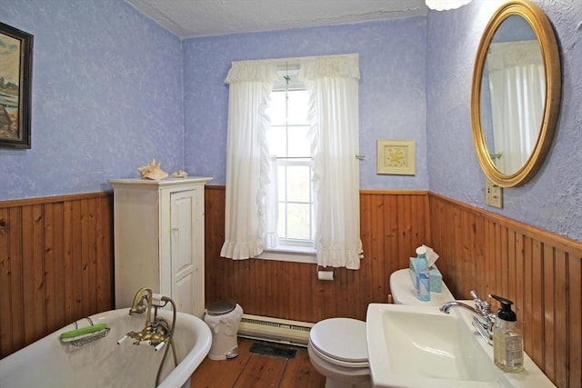 bathroom with wood finished floors, wainscoting, a baseboard heating unit, a freestanding tub, and a sink