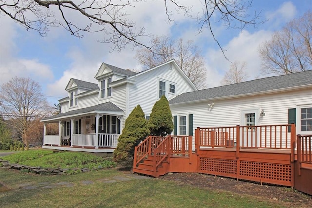 rear view of house featuring a deck, a yard, and roof with shingles