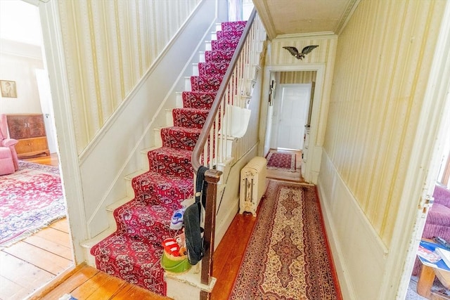 staircase with crown molding and wood finished floors
