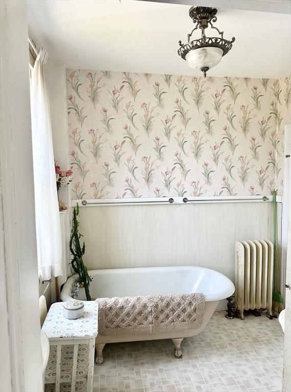 bathroom featuring radiator heating unit, a soaking tub, wainscoting, and wallpapered walls