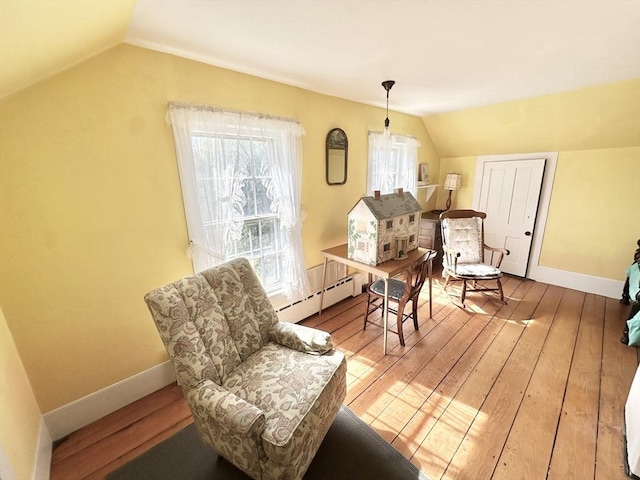 living area with baseboards, baseboard heating, vaulted ceiling, and hardwood / wood-style floors