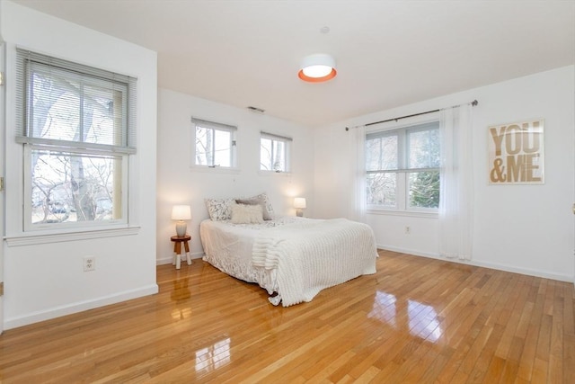 bedroom with multiple windows, baseboards, and light wood finished floors