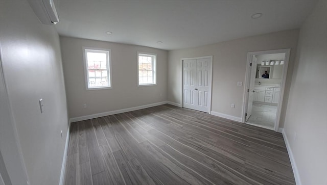 unfurnished bedroom with a closet, wood finished floors, ensuite bath, recessed lighting, and baseboards