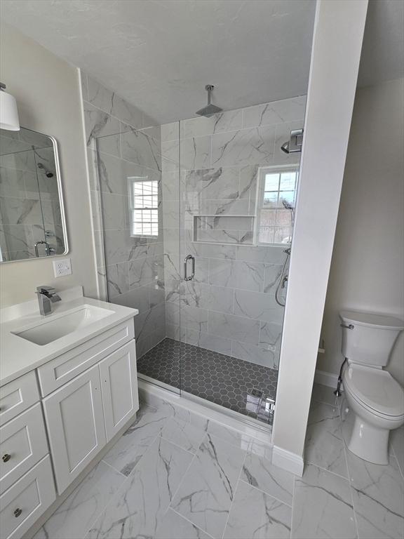bathroom featuring a stall shower, toilet, marble finish floor, baseboards, and vanity