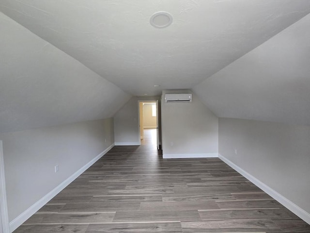 additional living space featuring lofted ceiling, baseboards, wood finished floors, and an AC wall unit