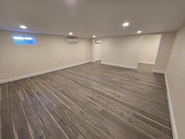 below grade area featuring recessed lighting, dark wood-style flooring, baseboards, and an AC wall unit
