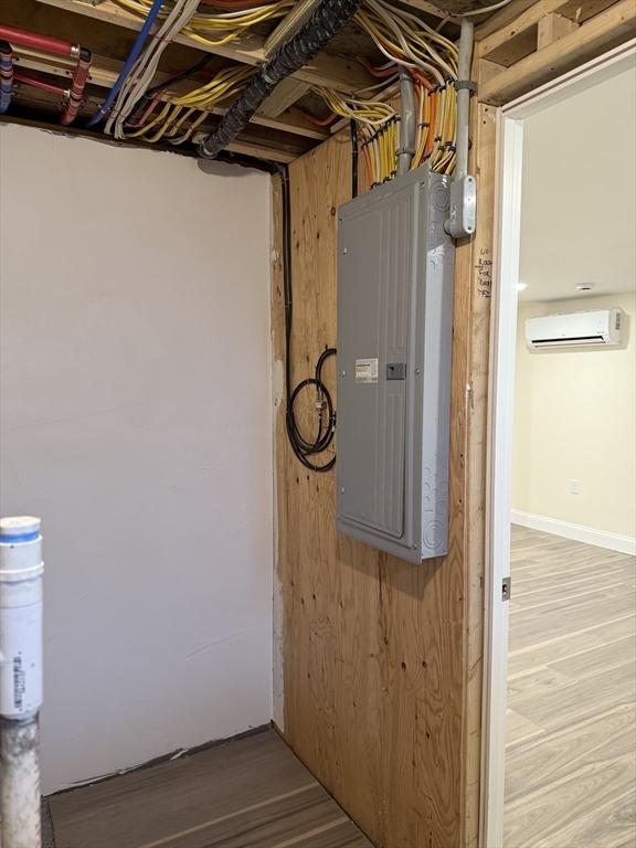 utility room featuring electric panel and a wall mounted air conditioner