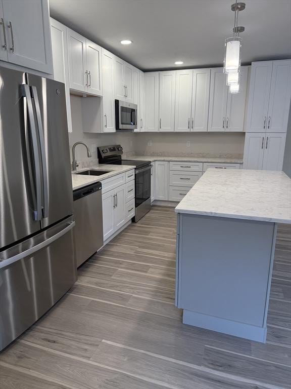 kitchen with wood finished floors, a sink, pendant lighting, white cabinetry, and appliances with stainless steel finishes