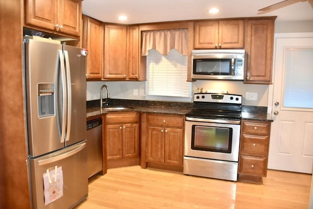 kitchen featuring appliances with stainless steel finishes, light hardwood / wood-style flooring, dark stone counters, and sink