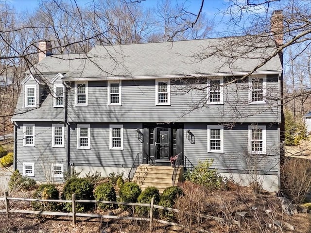 view of front of property with roof with shingles, a chimney, and fence