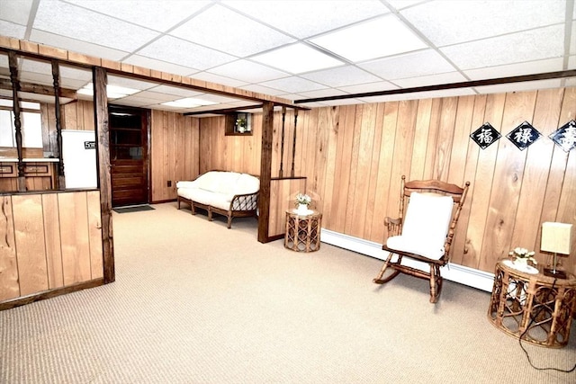 sitting room featuring carpet, wooden walls, and a paneled ceiling