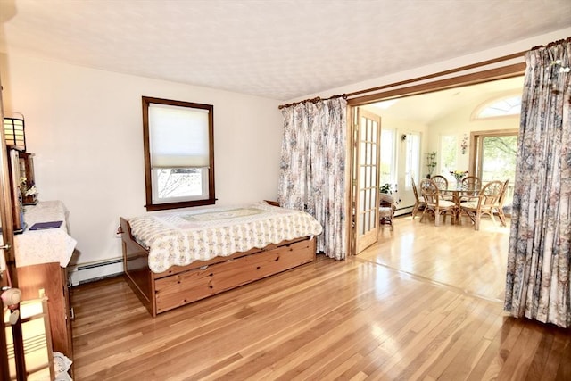bedroom featuring lofted ceiling, light wood finished floors, and a baseboard radiator