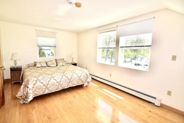 bedroom with multiple windows, wood-type flooring, and a baseboard heating unit