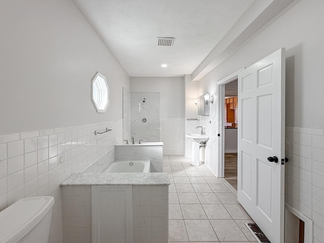 bathroom with toilet, a bathtub, a wainscoted wall, tile walls, and visible vents