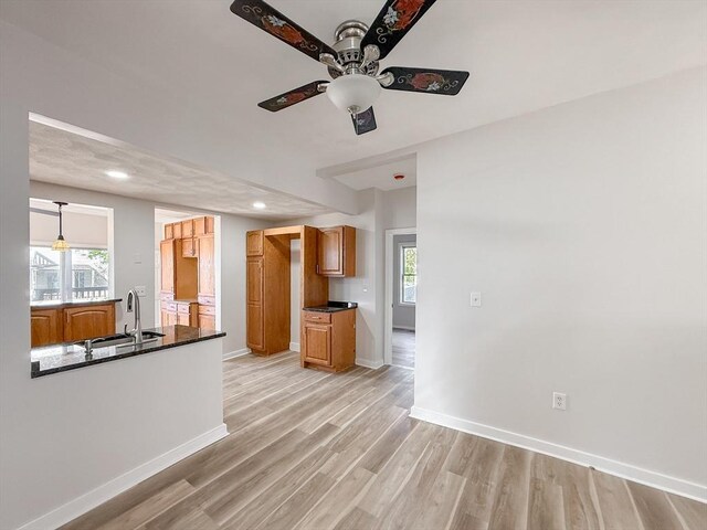 kitchen featuring ceiling fan, dark countertops, a sink, baseboards, and light wood-style flooring