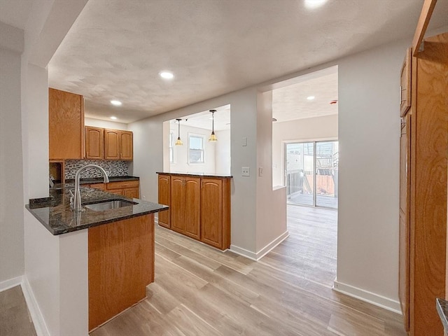 kitchen featuring brown cabinetry, a sink, baseboards, light wood finished floors, and a wealth of natural light