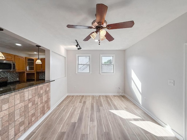 unfurnished living room featuring light wood-type flooring, baseboards, and ceiling fan
