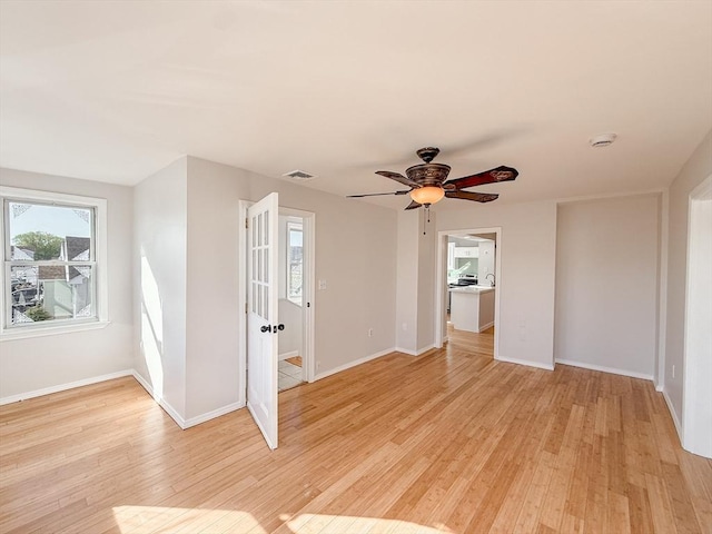 empty room with baseboards, light wood finished floors, ceiling fan, and visible vents