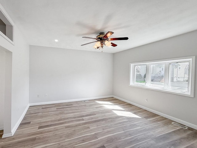 empty room featuring ceiling fan, visible vents, baseboards, and light wood finished floors