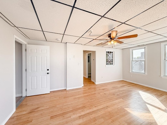 empty room with a paneled ceiling, baseboards, and light wood-style flooring
