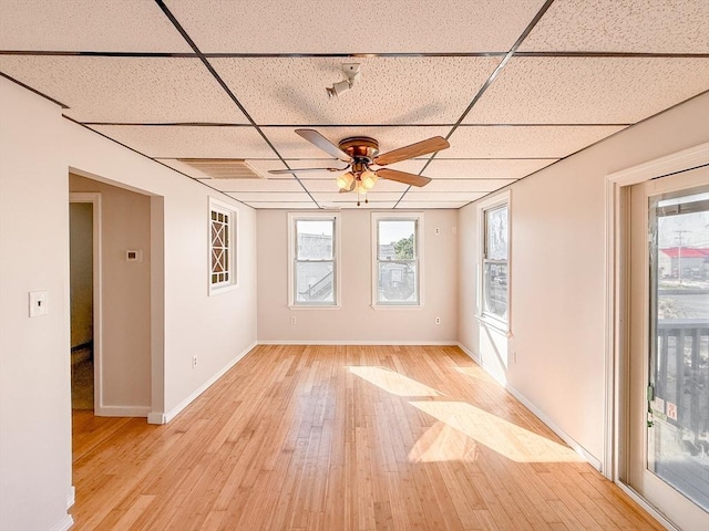 empty room featuring baseboards, a drop ceiling, a ceiling fan, and light wood-type flooring