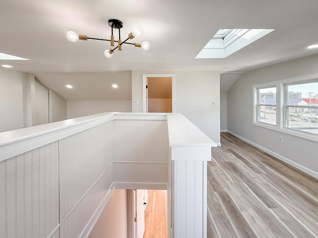 hallway featuring an inviting chandelier, baseboards, a skylight, light wood finished floors, and an upstairs landing