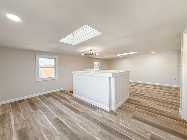 spare room featuring a skylight, a healthy amount of sunlight, baseboards, and light wood-style flooring