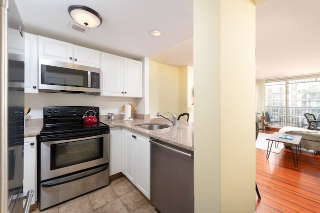 kitchen with sink, light hardwood / wood-style flooring, light stone counters, white cabinetry, and stainless steel appliances