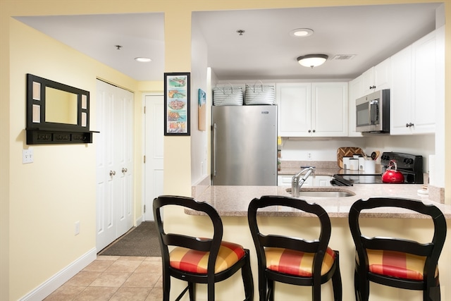 kitchen with appliances with stainless steel finishes, sink, light tile patterned floors, white cabinets, and a breakfast bar area