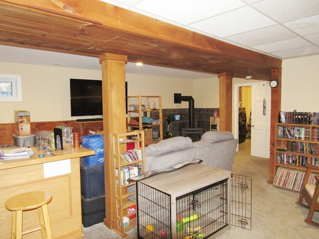 living room with a paneled ceiling, light colored carpet, a wood stove, and wood walls