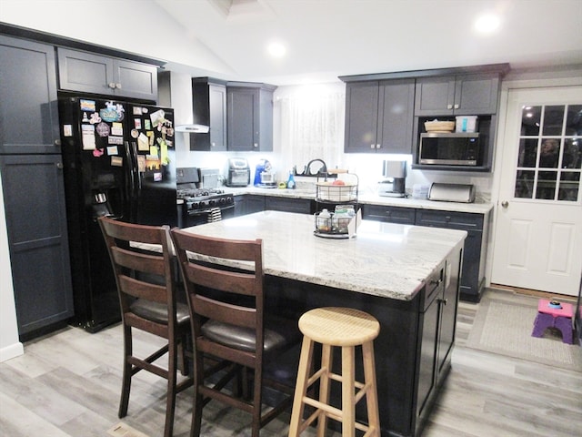 kitchen with a breakfast bar, a center island, lofted ceiling, black appliances, and light wood-type flooring