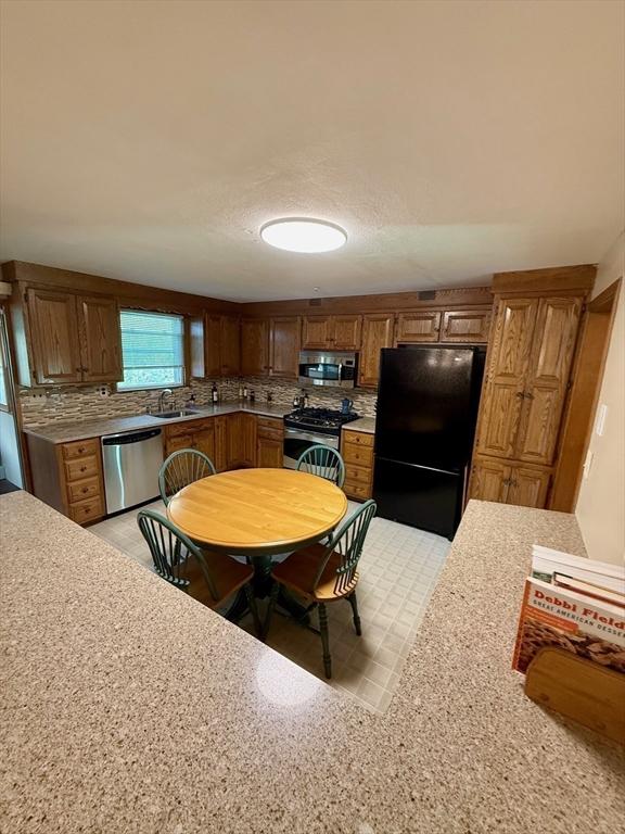 4 Fernandez Cir, Randolph, MA 02368 - kitchen with stainless steel appliances, a sink, light countertops, brown cabinetry, and decorative backsplash