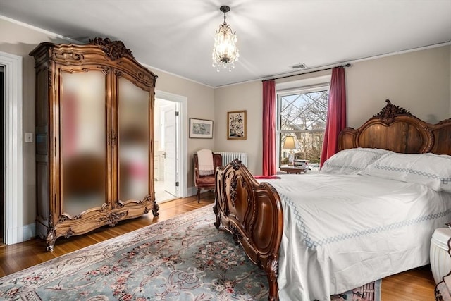 bedroom with radiator, ensuite bath, wood-type flooring, and a chandelier