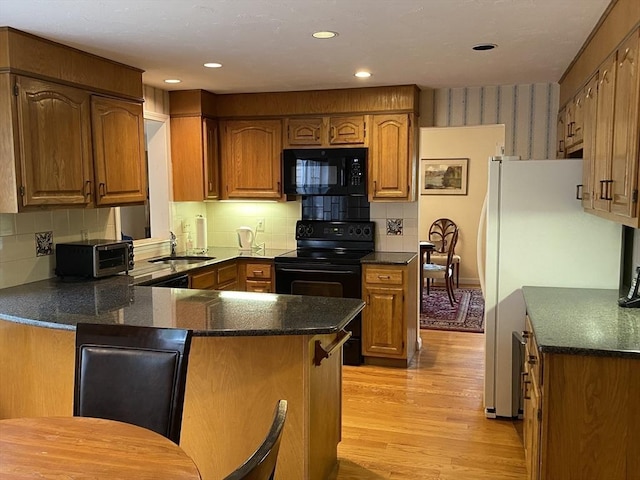 kitchen with black appliances, a peninsula, a sink, light wood finished floors, and tasteful backsplash