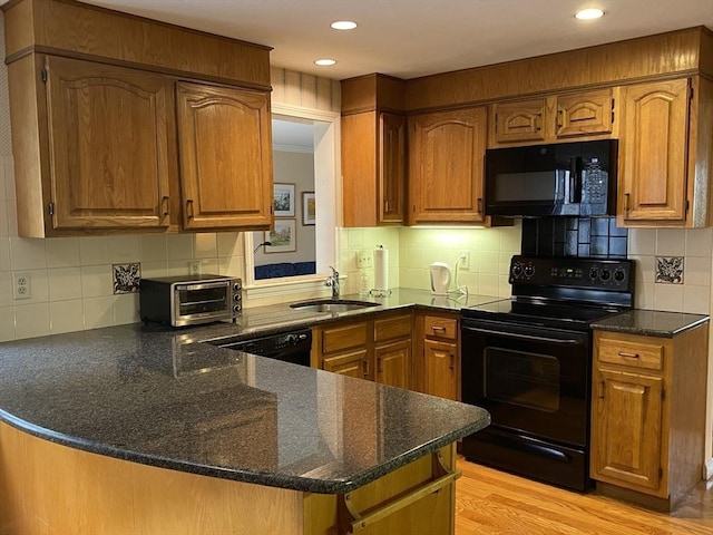 kitchen with black appliances, a sink, brown cabinets, a peninsula, and light wood-style flooring