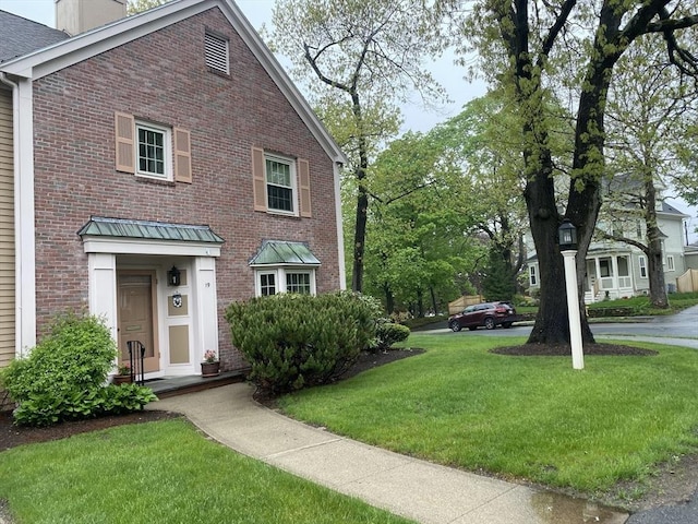 view of front of house featuring a chimney, a front lawn, and brick siding