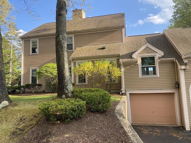 traditional-style home featuring a chimney, a garage, asphalt driveway, and a shingled roof
