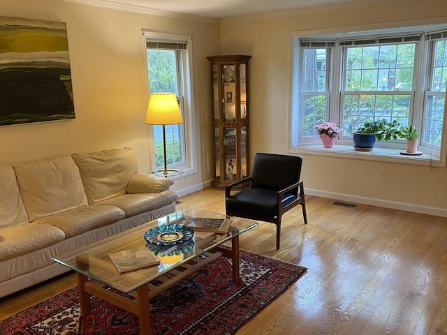 living area with crown molding, baseboards, and light wood finished floors