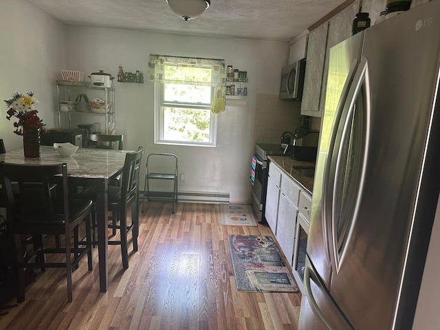 26 Burnap Rd Unit 6, Holliston, MA 01746 - kitchen with stainless steel appliances, light wood finished floors, a textured ceiling, decorative backsplash, and a baseboard radiator