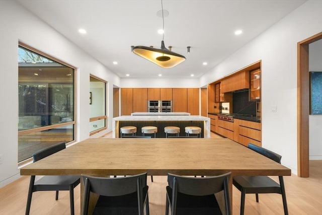 kitchen featuring stainless steel gas stovetop, light wood-type flooring, a kitchen bar, and decorative light fixtures