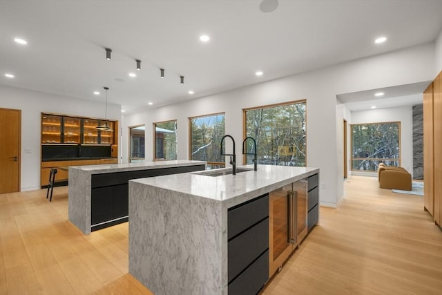 kitchen featuring pendant lighting, sink, light hardwood / wood-style flooring, and an island with sink