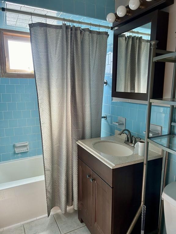 full bathroom with tile walls, backsplash, shower / tub combo, vanity, and tile patterned flooring