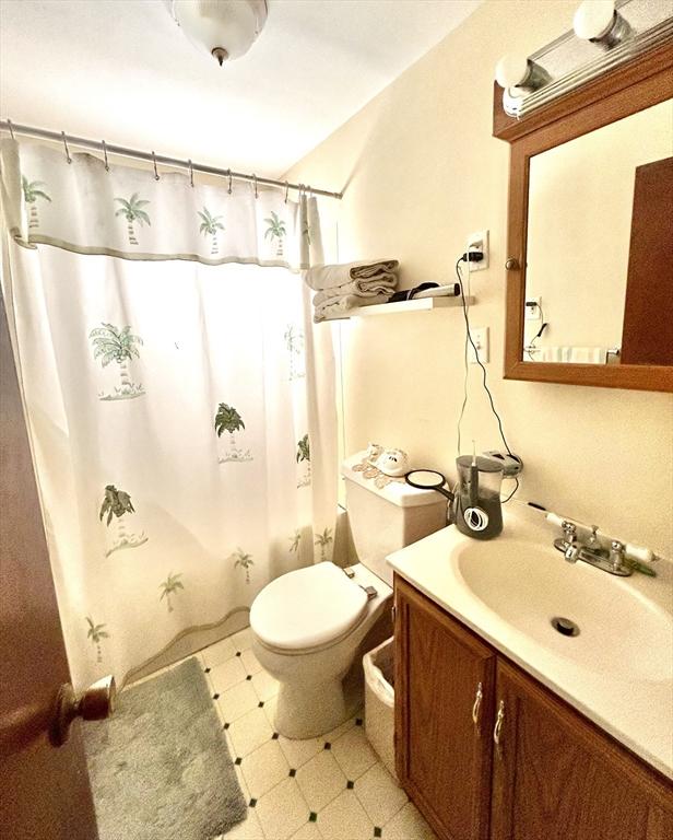 bathroom featuring toilet, lofted ceiling, shower / tub combo with curtain, tile patterned floors, and vanity