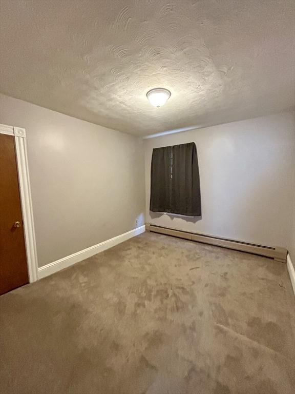 carpeted empty room with a baseboard radiator, a textured ceiling, and baseboards