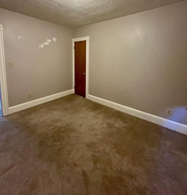 empty room with a textured ceiling, dark colored carpet, and baseboards