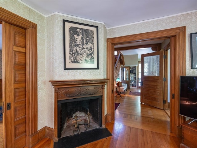 living room featuring wallpapered walls, wood finished floors, a fireplace with flush hearth, and ornamental molding