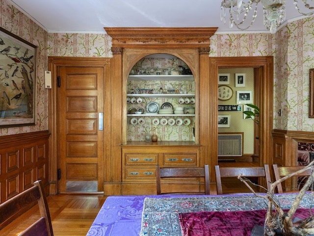 dining space featuring wallpapered walls, a chandelier, crown molding, wood finished floors, and wainscoting