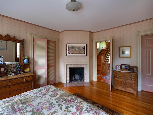 bedroom featuring crown molding, wood finished floors, wallpapered walls, a tile fireplace, and a closet