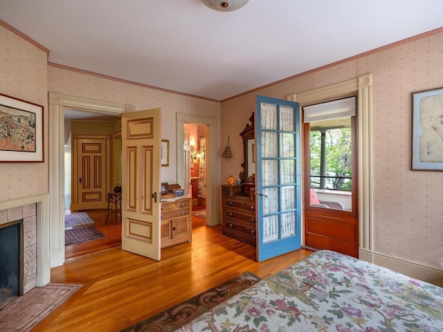 bedroom with ornamental molding, wallpapered walls, light wood-type flooring, and a tiled fireplace