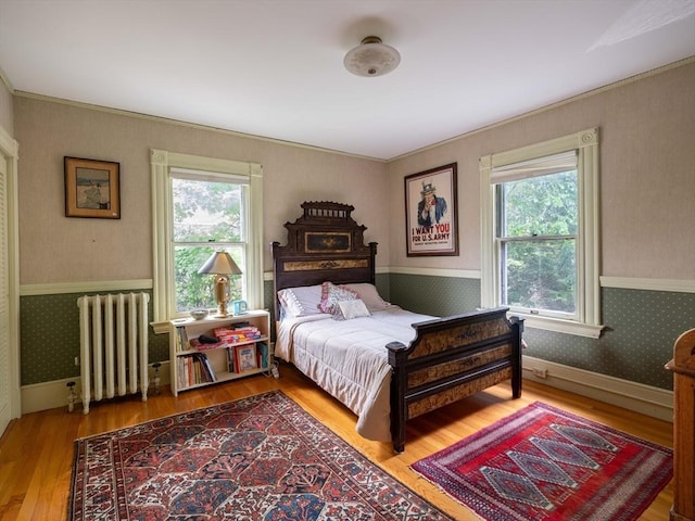 bedroom with radiator heating unit, wallpapered walls, a wainscoted wall, multiple windows, and wood finished floors